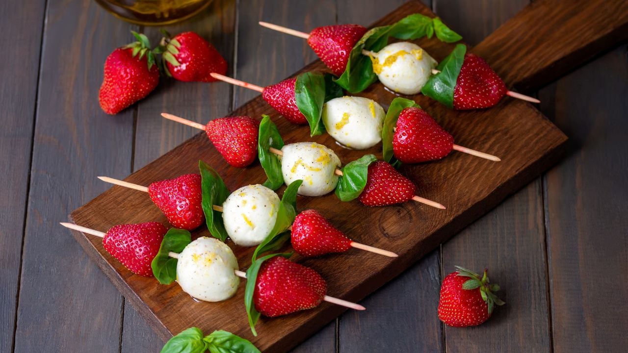 Strawberry Caprese Skewers. Lemon olive oil marinated mozzarella mini balls with fresh basil leafs and strawberries threaded on skewers served on a wooden board. Selective focus, horizontal.