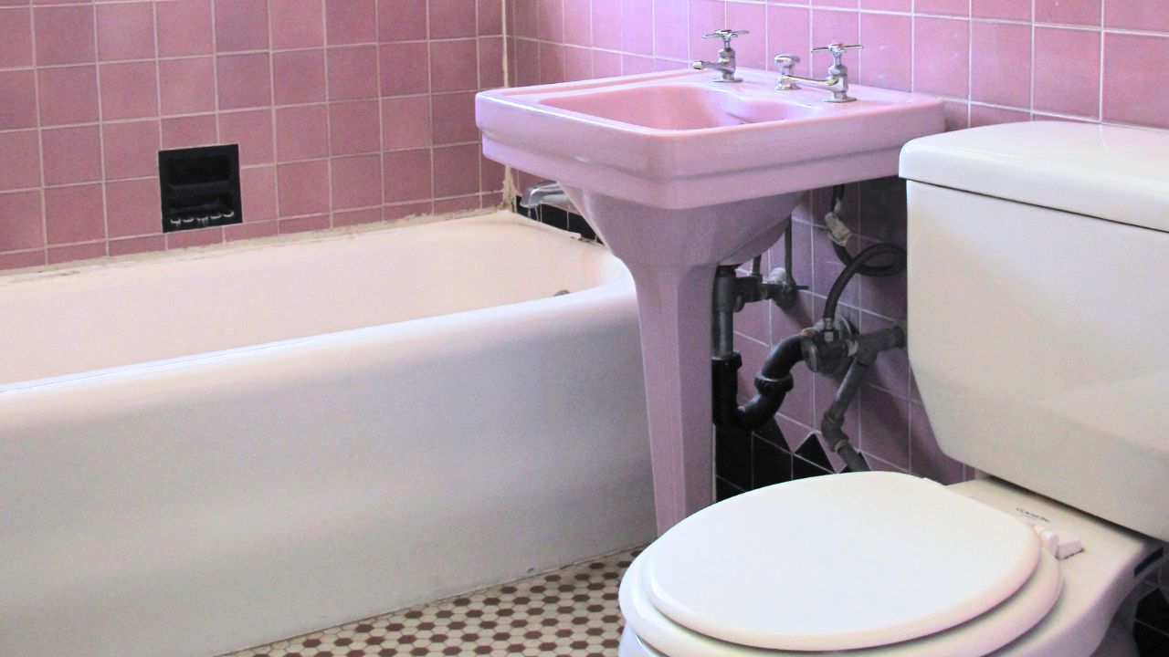 Bathroom in 1920s apartment house with original enlight thulian pink and black tile, hexagonal floor tiles, and pedestal sink. Location is Los Angeles, California.