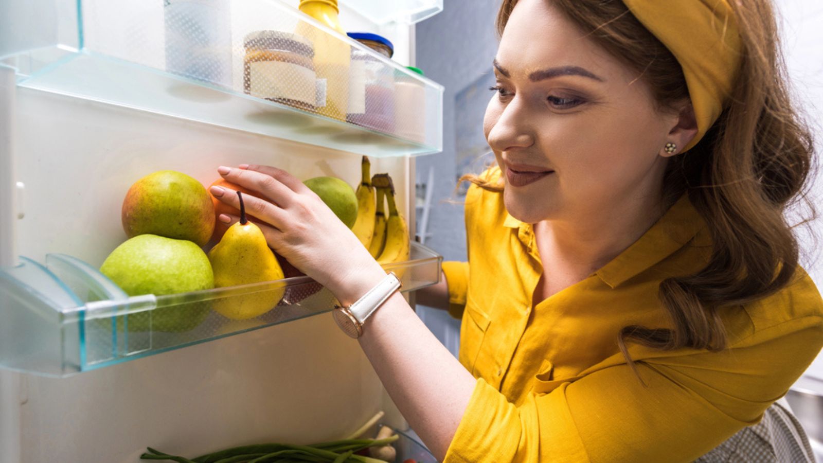 Beautiful woman taking fruits from fridge at kitchen