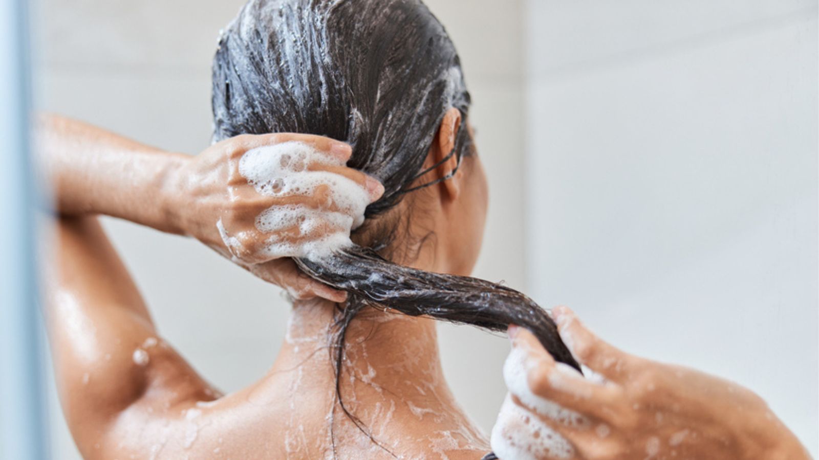Brunette young woman washing her hair in shower