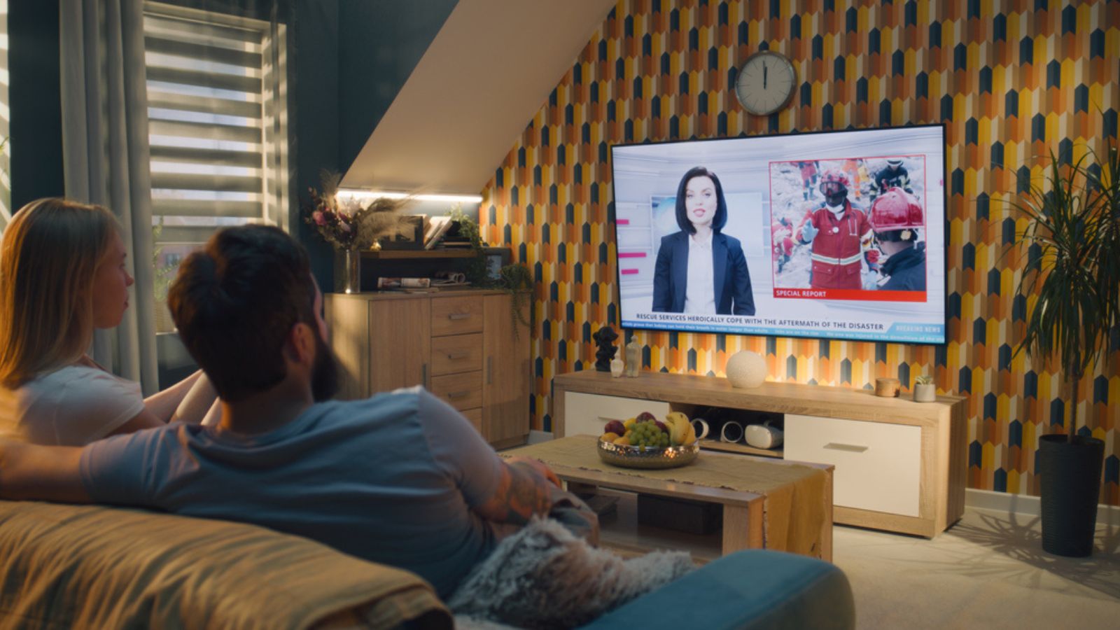 Couple sitting on sofa in living room together, talking, watching TV news about disaster