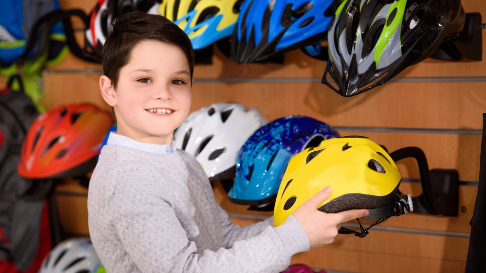 Cute little boy holding bicycle helmet and smiling at camera in bike shop