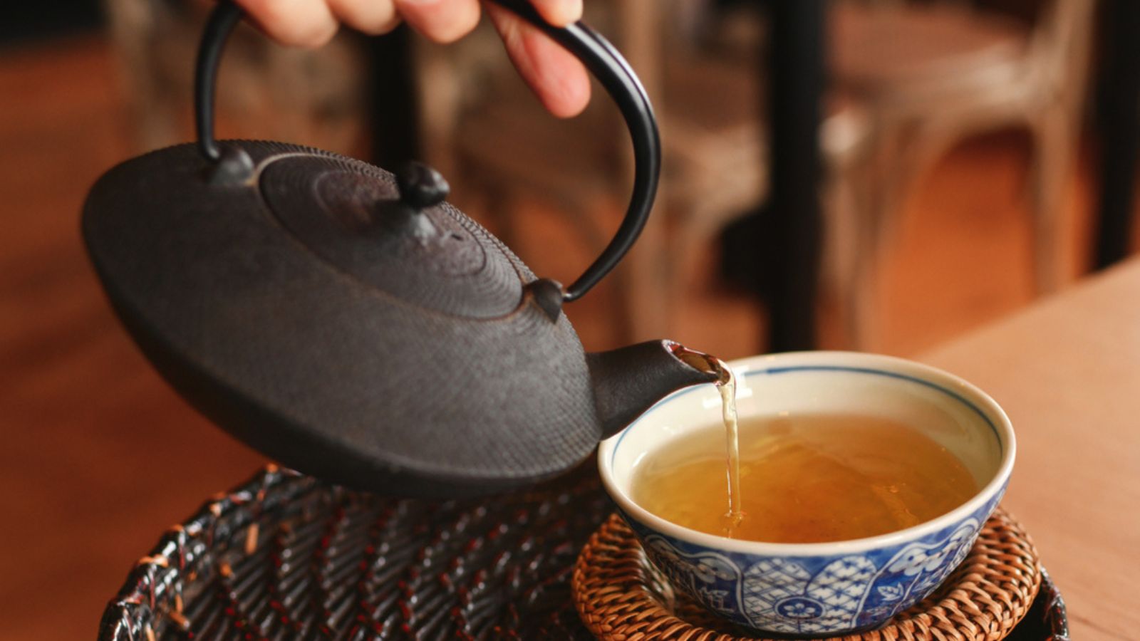 Hand pours green tea from a cast iron teapot into a cap
