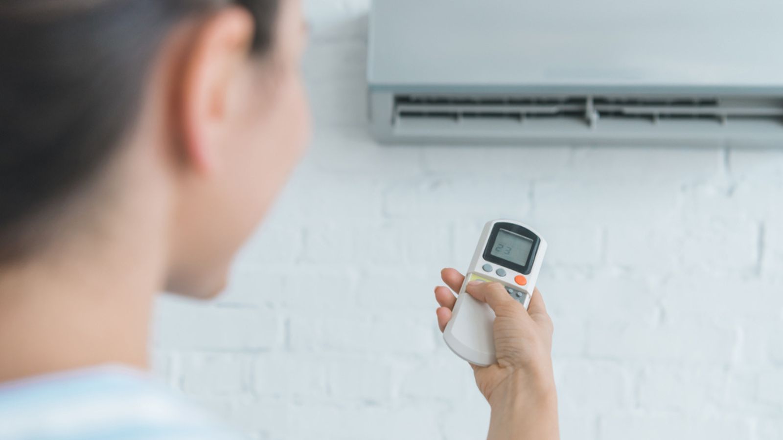 Selective focus of woman with remote control turning on air conditioner