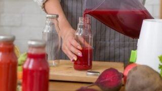 Healthy, weight loss food concept. Woman in linen apron pouring beet detox juice into bottle at home