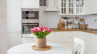 A bouquet of tulips on a white table. In the background, the interior of a white kitchen in the Scandinavian style. The concept of home comfort.The concept of International Women's Day on March 8.