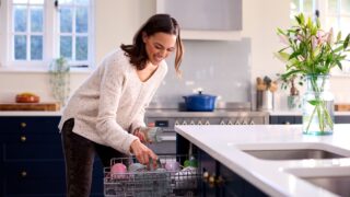 Woman Doing Chores Loading Dishwasher In Kitchen At Home