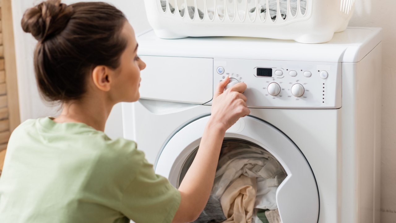 Side view of blurred woman switching washing machine near basket in laundry room