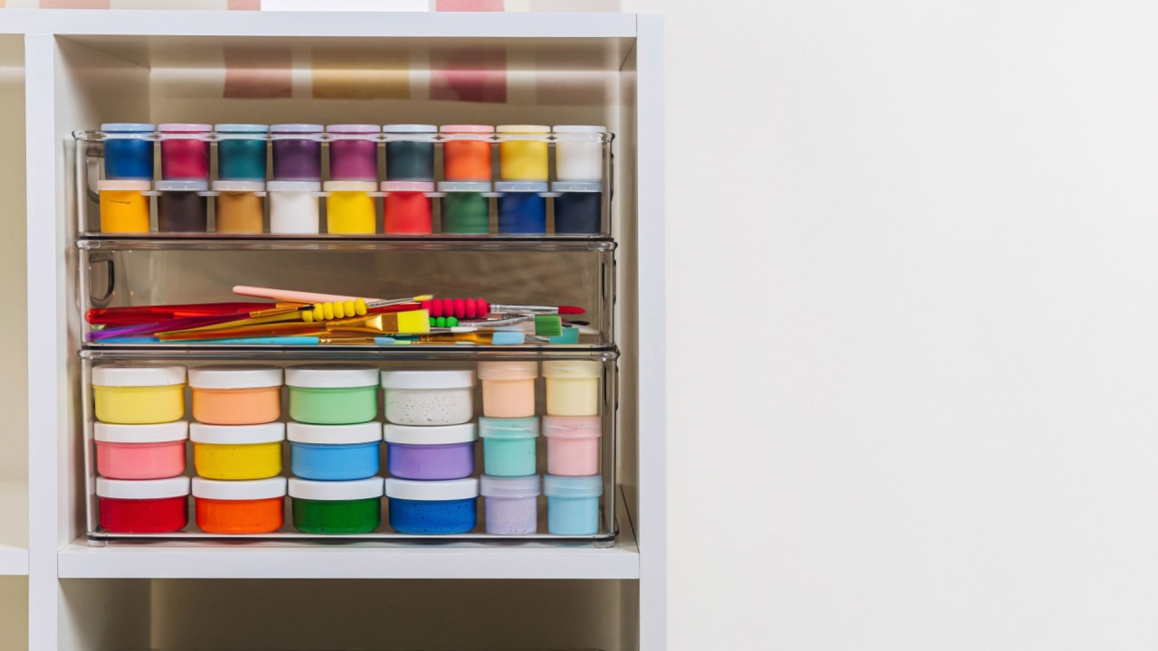 Transparent plastic containers with stationery and supplies for drawing and craft on shelves. White shelving with various material for creativity and art activity. Organizing and storage craft room.