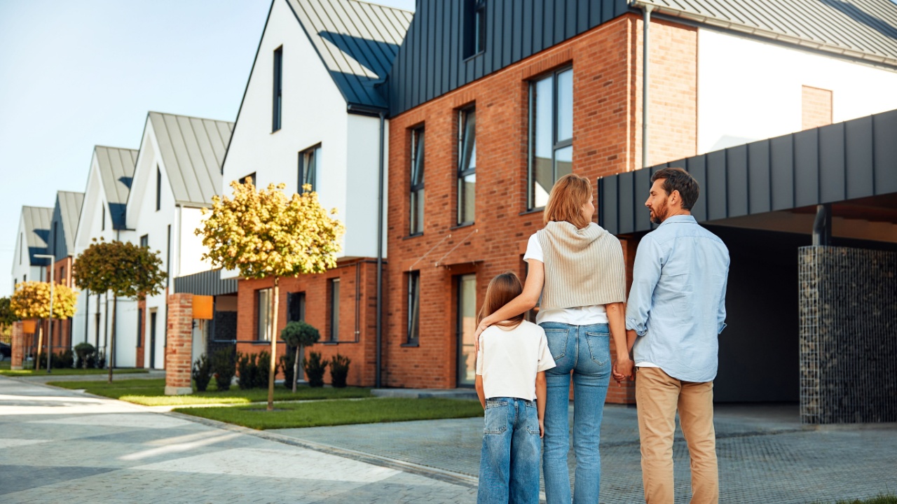 A young happy family with a child hugging each other are standing and looking on the street at their new home. Renting and buying real estate. Moving concept.