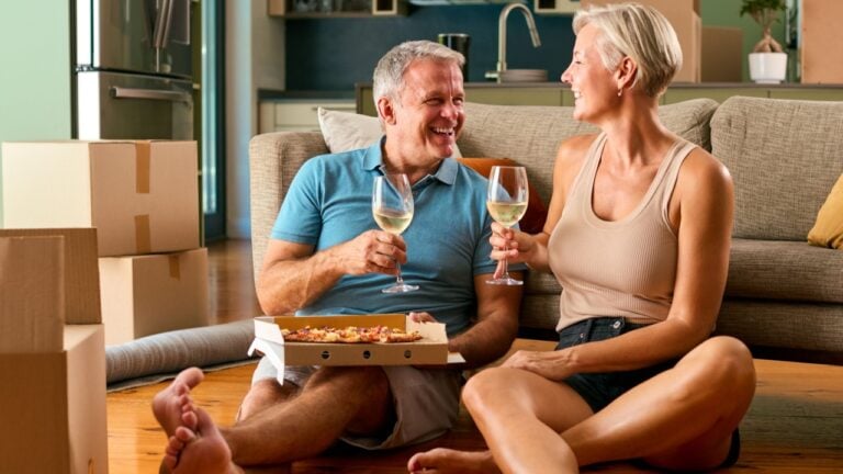 Mature Couple Celebrating In New Home On Moving Day Eating Pizza And Drinking Wine