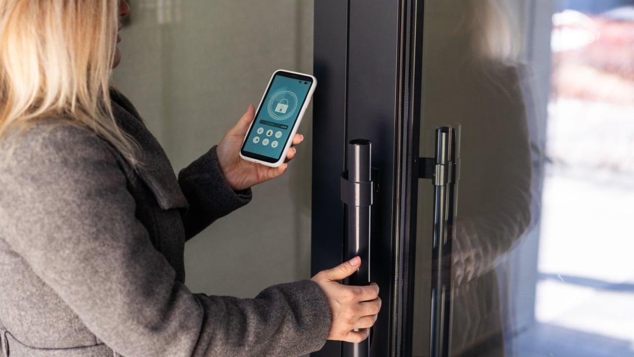Woman locking smartlock on the entrance door using a smart phone. Concept of using smart electronic locks with keyless access.