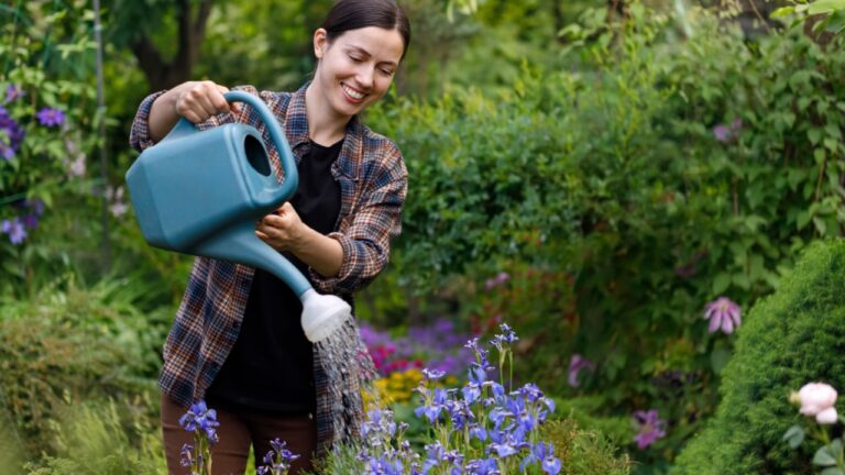smiling young woman gardener water the flowers from watering can in garden. Hobby concept of growing and taking care of plants at backyard