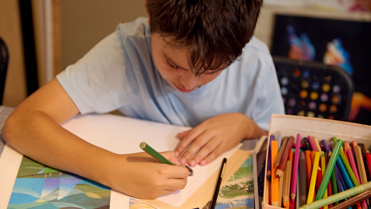 Kids have art class, drawing, painting with teacher in workshop. A young boy focuses on his artwork, surrounded by colorful pencils and paper.