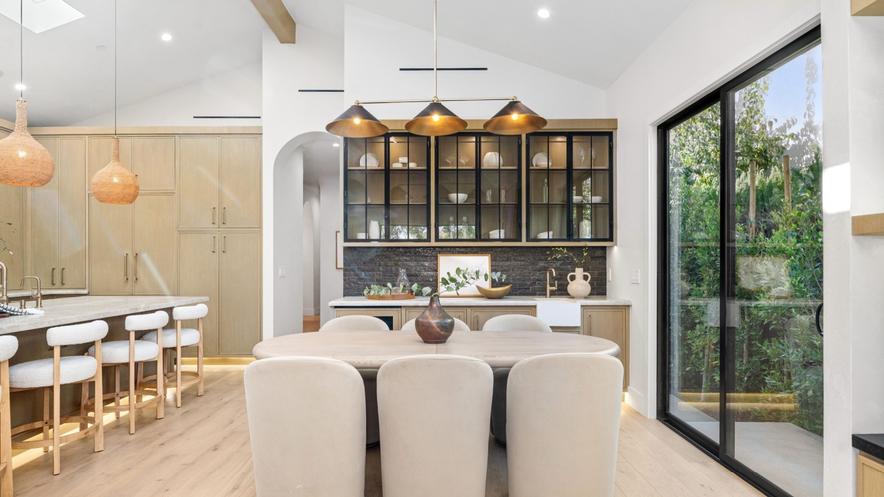 Modern kitchen interior with wooden cabinets, island seating, and large windows overlooking greenery.