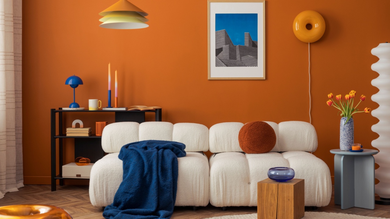 Modern cozy living room with white boucle sofa, orange wall and eclectic decor in bold colors.