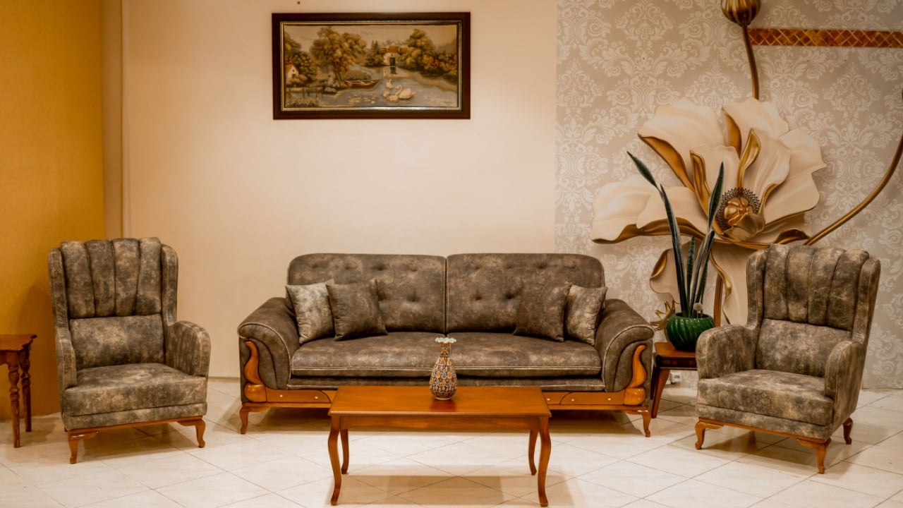 Vintage living room furniture set in olive green upholstery with a traditional wooden coffee table and matching high-back armchairs. The setup is completed with soft lighting and floral wall art
