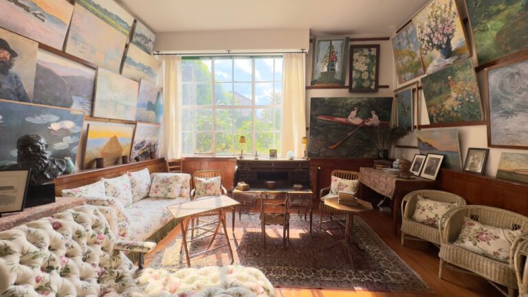 Giverny, France - 06082025: Interior of a room densely decorated with paintings, featuring furniture, floral upholstery, a desk, and a large window.
