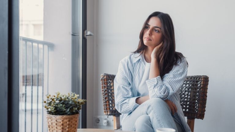 Anxiety woman in stress, looking aside nervously squeezes hands sitting on sofa thinking about problems after receive bad news on cellphone. Worried female feel frustration waiting call on smartphone.
