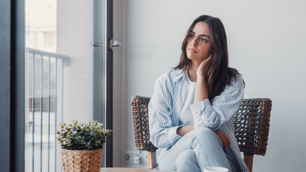 Anxiety woman in stress, looking aside nervously squeezes hands sitting on sofa thinking about problems after receive bad news on cellphone. Worried female feel frustration waiting call on smartphone.