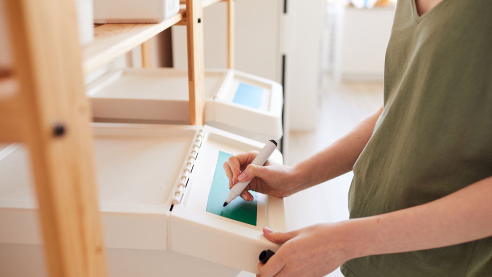 Side view close up of unrecognizable woman labeling plastic bins at home while managing storage and waste sorting at home, copy space