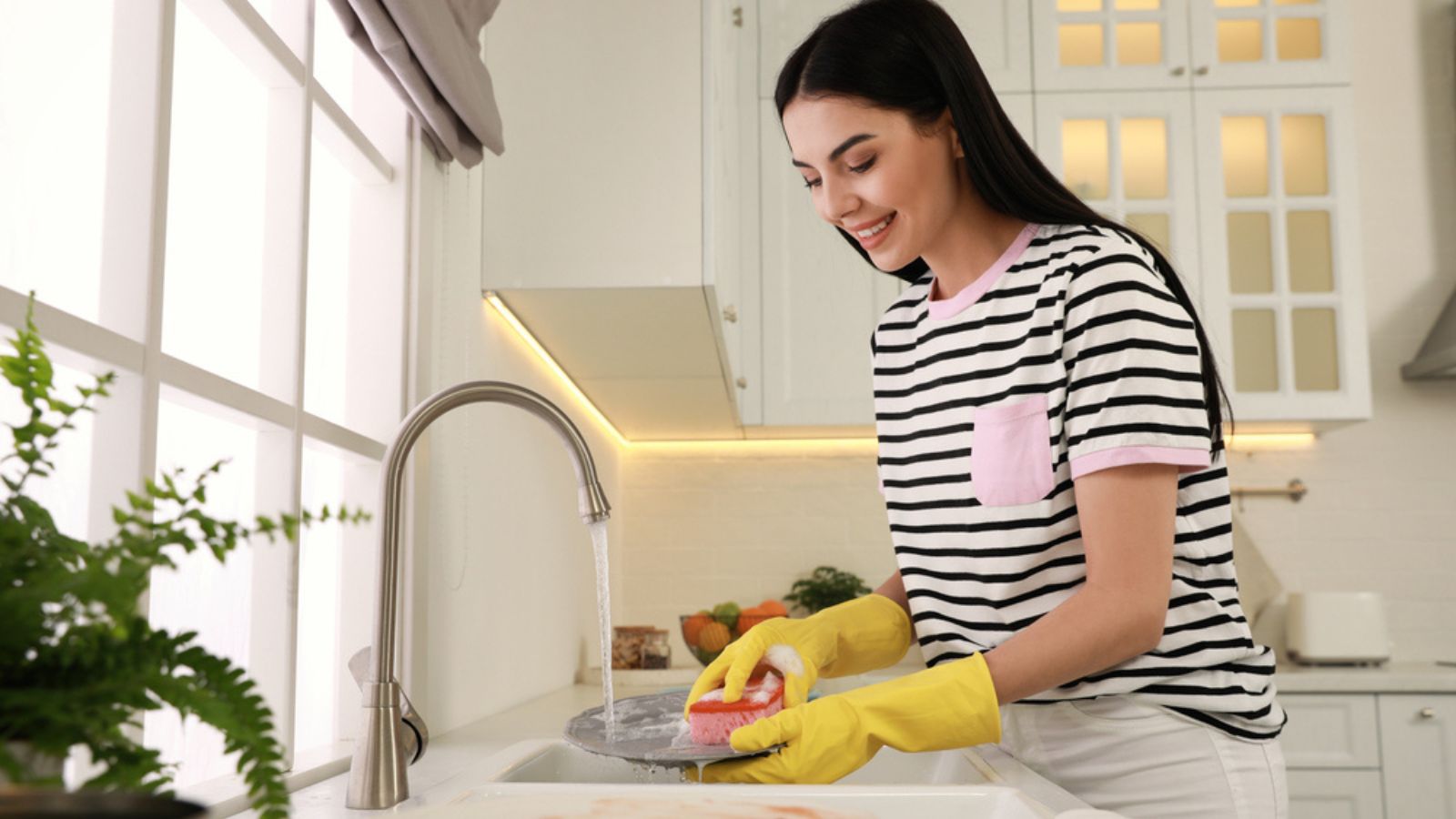 Woman washing plate above sink in kitchen