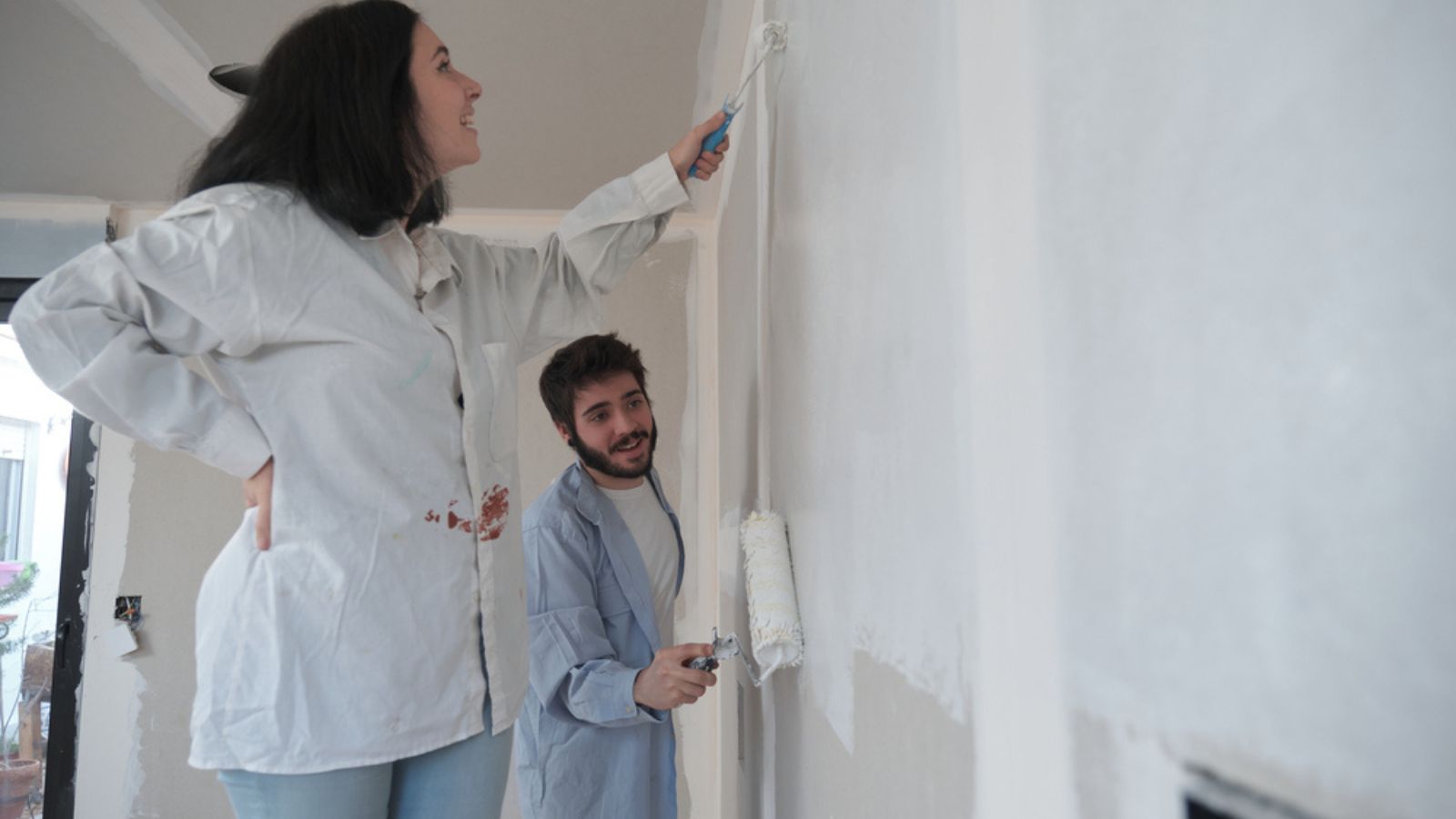 Young couple painting walls and smiling in their new house in construction.