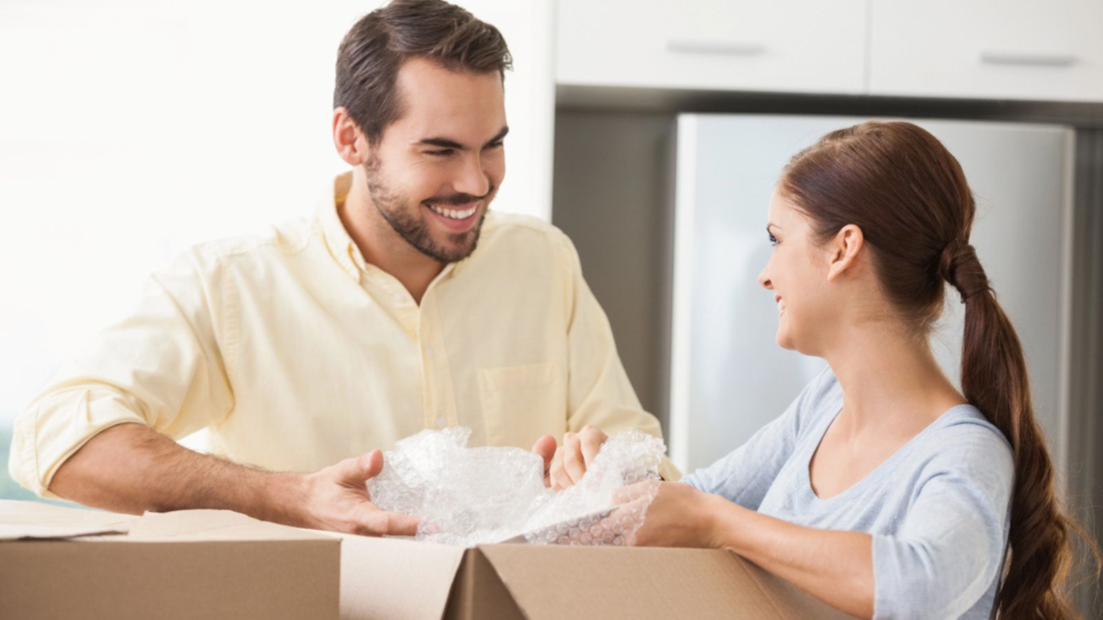 Young couple unpacking boxes in kitchen in their new home. holding a bubble wrap