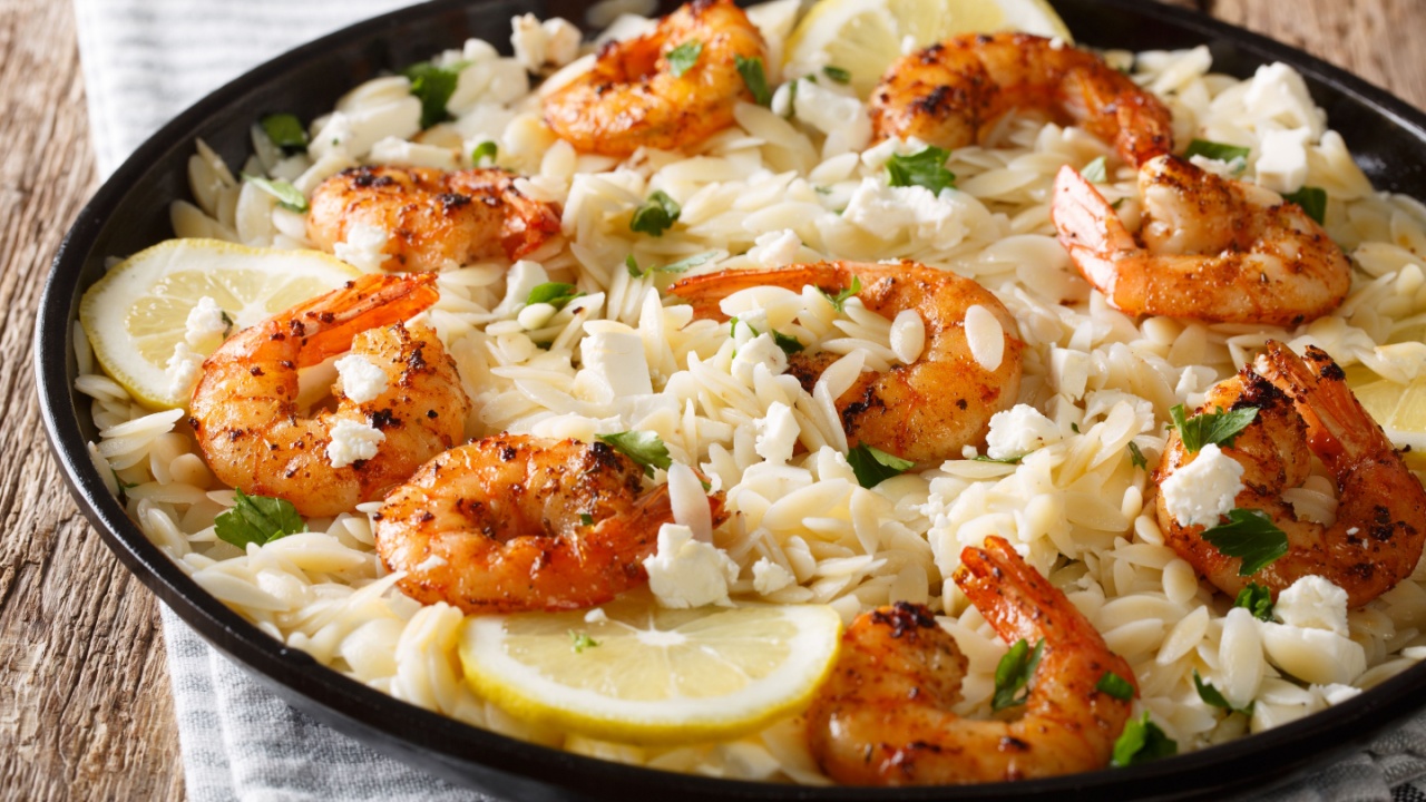 Spicy orzo pasta with grilled shrimps, feta cheese, herbs and lemon close-up on a plate on the table. horizontal