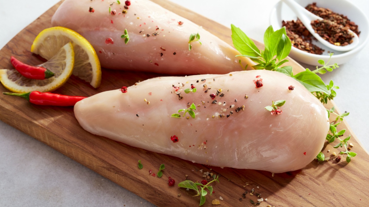 Seasoned skinless raw chicken breasts on a board sprinkled with chili flakes and spices, fresh herbs and lemon