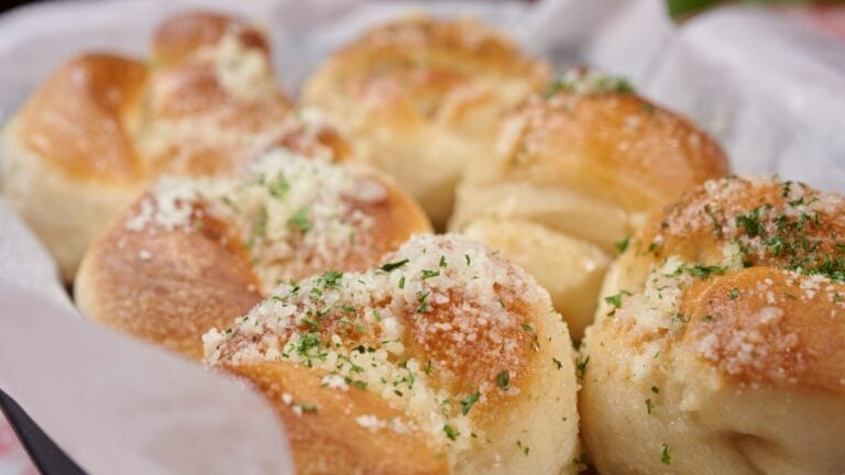 Garlic knots with Parmesan cheese and dried greens on top in a basket