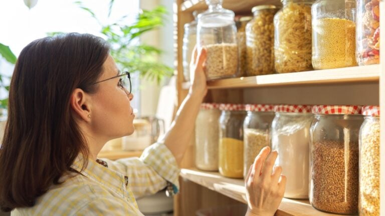 Food storage, wooden shelf in pantry with grain products in storage jars. Woman taking food for cooking