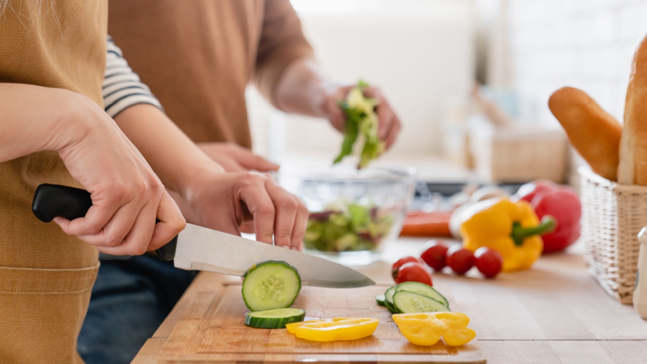 Close up cropped image of cutting board and couple cutting vegetables in the kitchen together, preparing food meal at home. Vegetarian healthy food