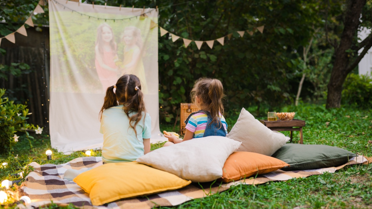 Backyard Family outdoor movie night with kids. Sisters spending time together and watching cimema at backyard. DIY Screen with film. Summer outdoor weekend activities with children. Open air cinema.