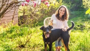 Young beautiful woman enjoying spring while sitting in a blooming garden playing with a dog on a summer day