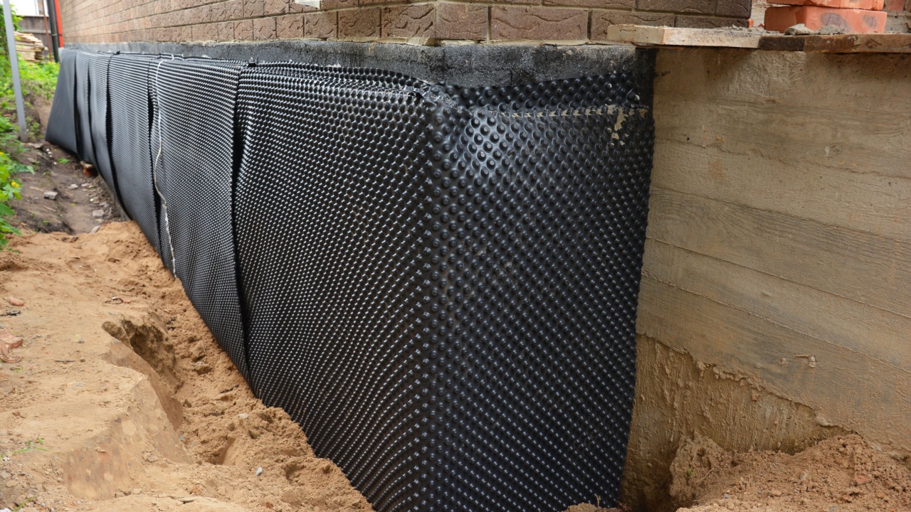 House foundation waterproofing. Installation of a dimpled waterproofing membrane on the exterior brick house basement wall.