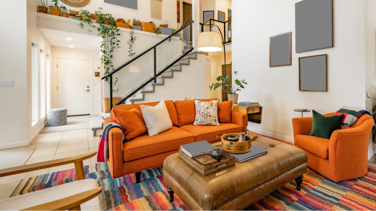 Bohemian style living room with orange sofa colored chairs books houseplants stair case and cluttered decor