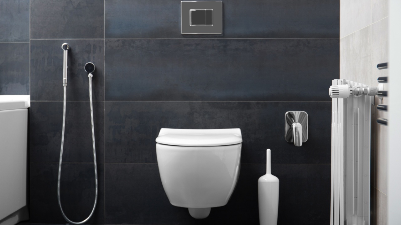 Modern wall-mounted white toilet bowl, chrome flush button and bidet hygienic shower against the background of a black bathroom wall. Part of the interior of the bathroom in the apartment.