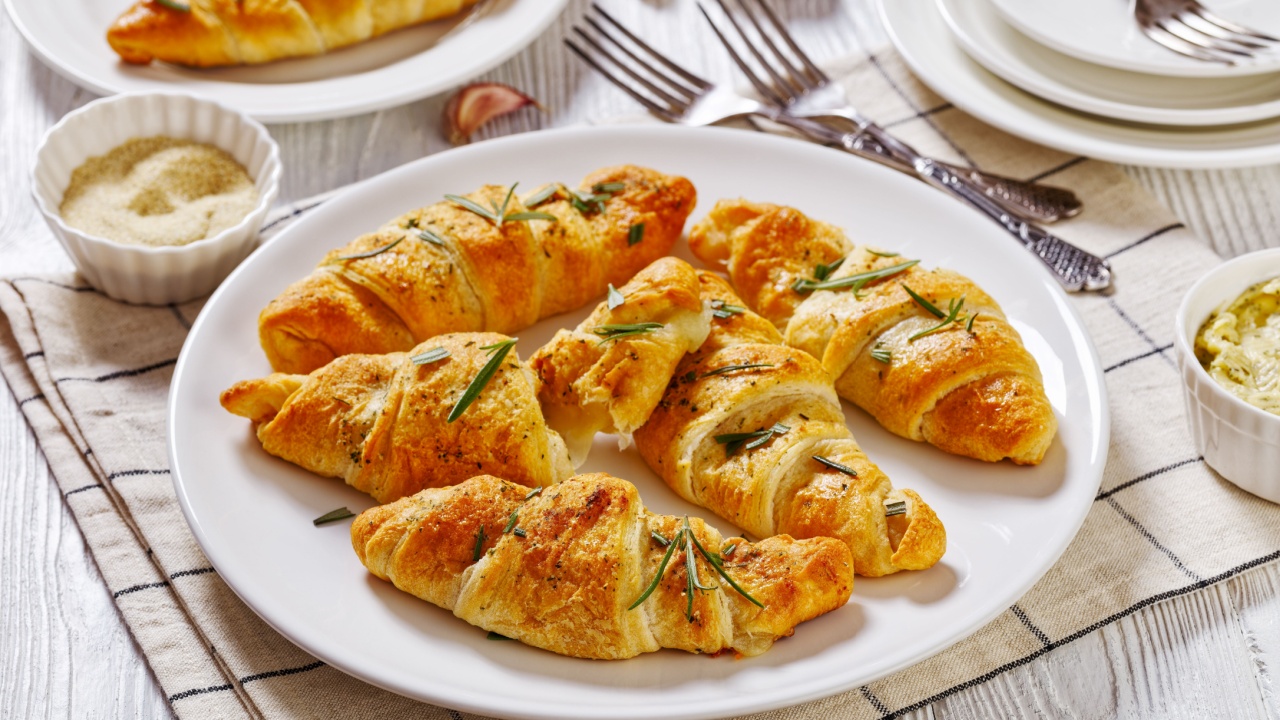 savory crescent rolls with garlic cheese filling, sprinkled with fresh rosemary leaves on white plate on white wooden table, horizontal view from above
