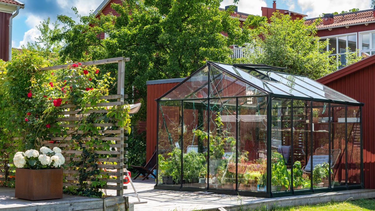 Beautiful greenhouse glass house in the garden yard near the villa. Wicker rattan chairs inside. Lots of pots with different plants. Greenhouse for growing plant seedlings. Landscape garden design.