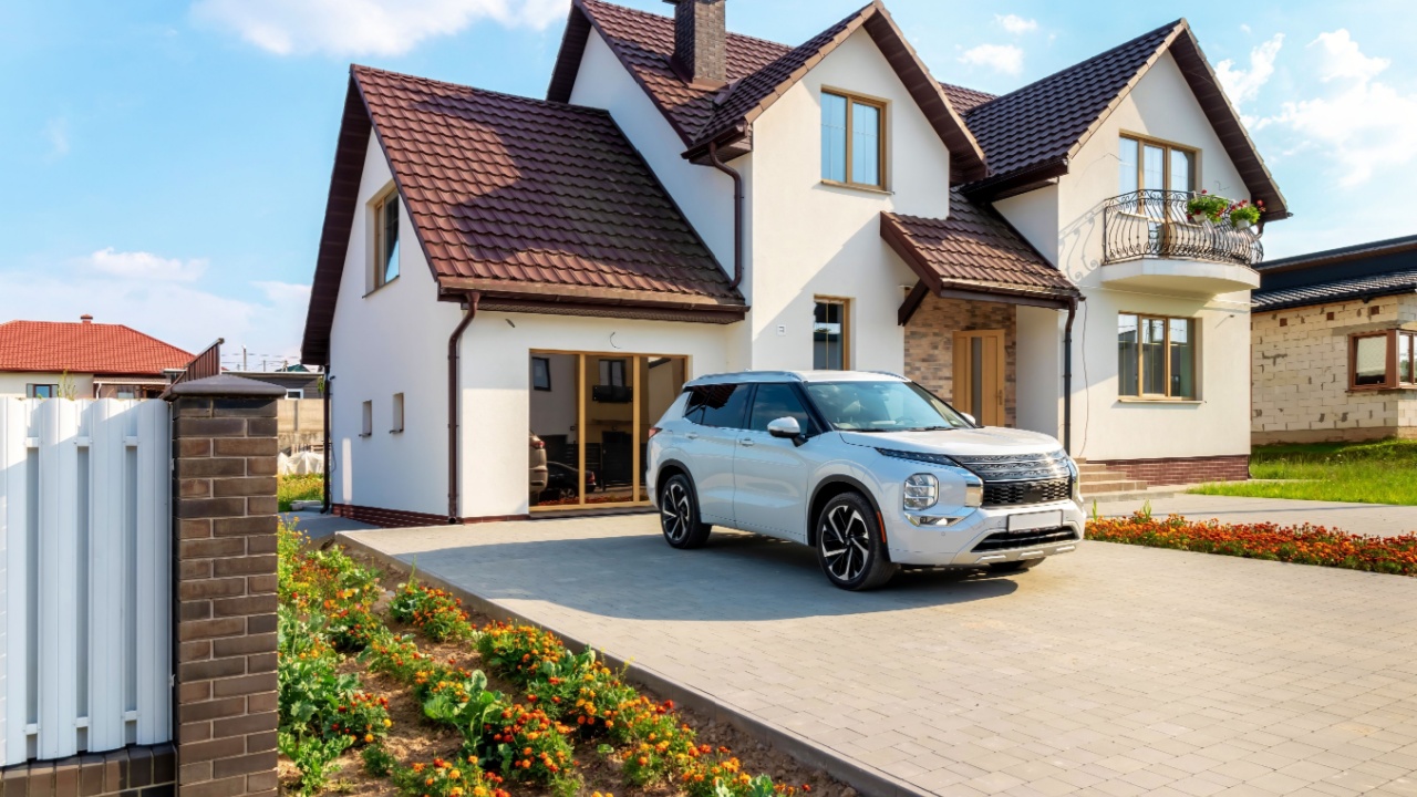 A white house with a flower bed and flowers, as well as a white car in front of the house.