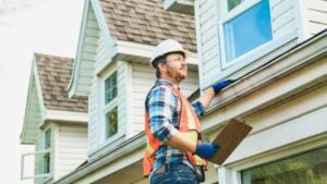 A man with hard hat standing on steps inspecting house roof
