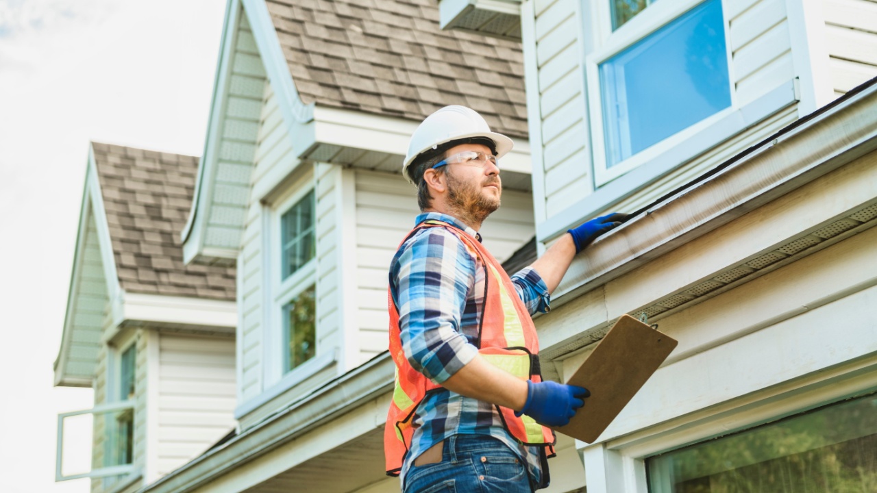 A man with hard hat standing on steps inspecting house roof