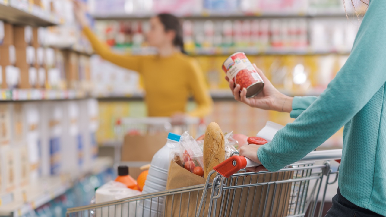 Woman putting items in the shopping cart at the grocery store, she is holding a can and reading the label