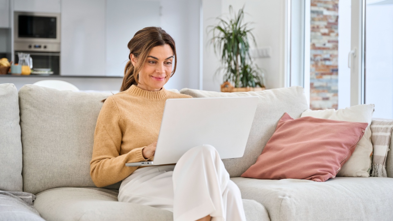 Happy mature older woman using laptop sitting on couch at home. Smiling middle aged 45 years old woman looking at computer browsing internet, doing shopping on website relaxing on sofa in living room.