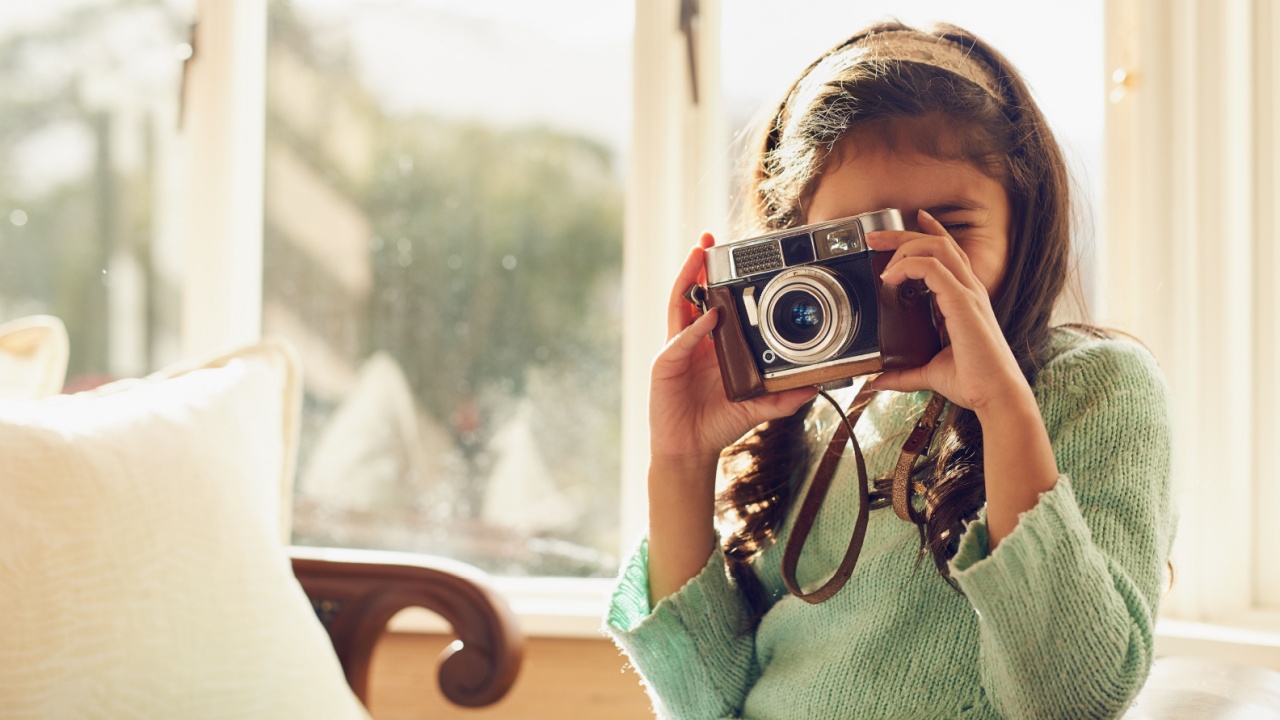 Home, girl and child with vintage camera, photography and memory with fun, playful and relax in living room. Apartment, retro or kid taking picture, creative and hobby with lens, learning or creative