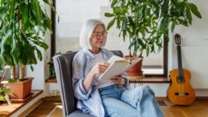 Beautiful mature woman reading book, feeling cozy and happy. Weekend activity for older woman, relaxing at home.