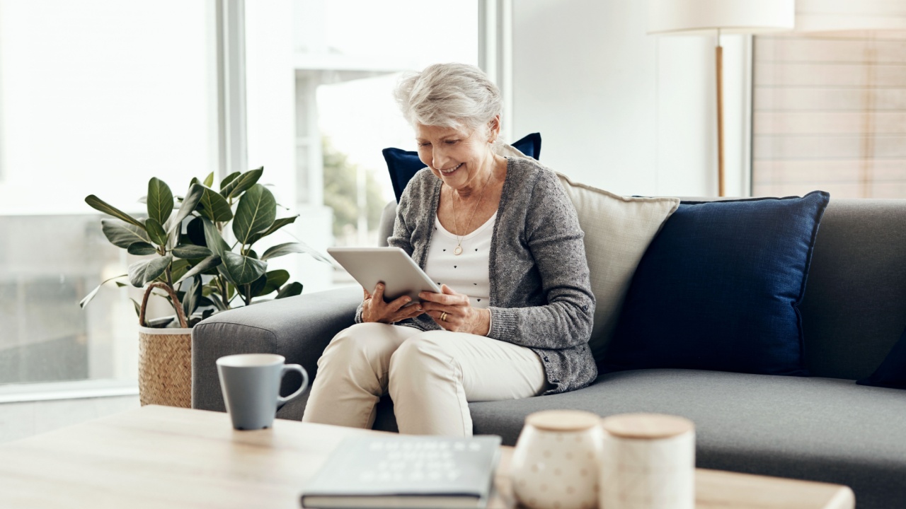 Senior woman, tablet and home with digital, game app or social media scroll for news in retirement. Lounge, sofa and smile with web, tech and relax in living room with series streaming at morning