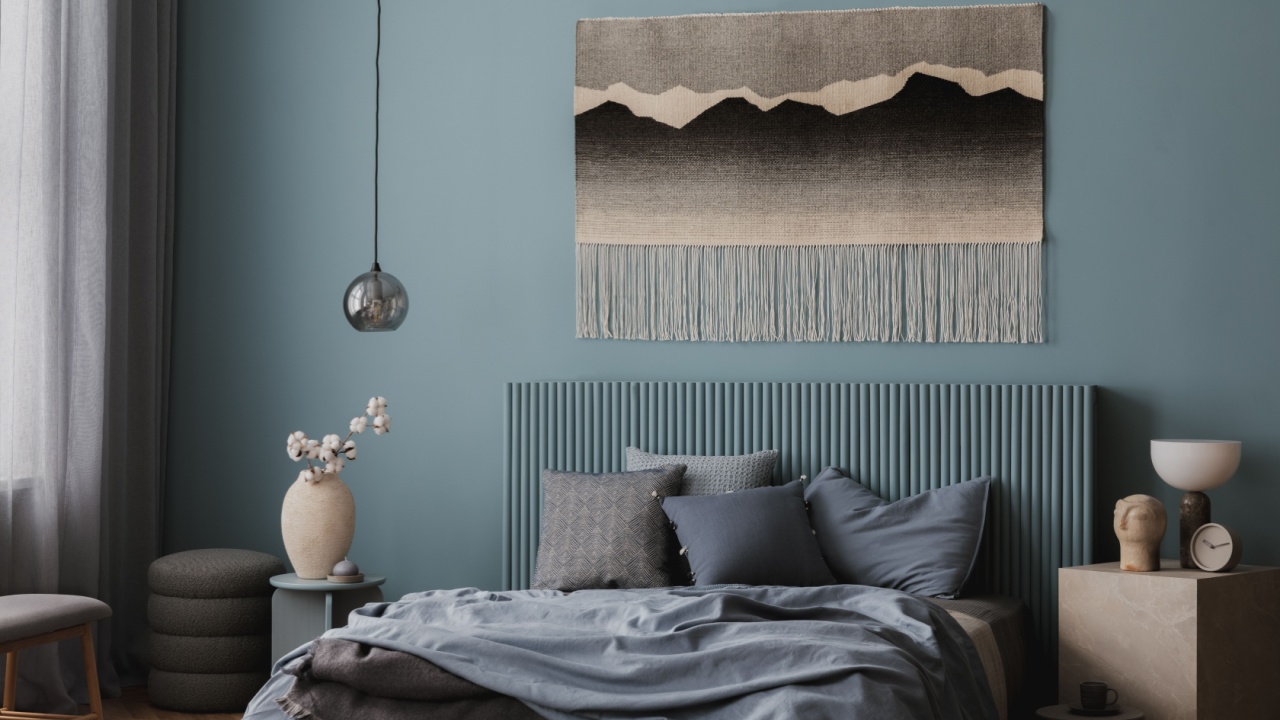 Stylish bedroom with a headboard in soft blue, a decorative woven tapestry, and an inviting bed with layered pillows and blankets.