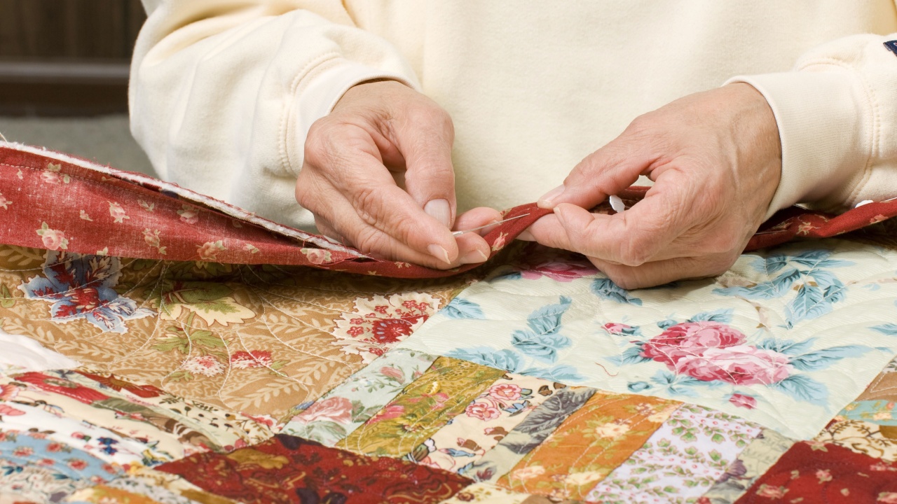 A woman stitches by hand the binding to finish a quilt.